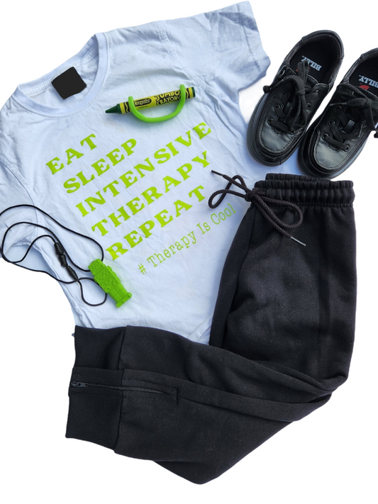 White Tshirt, Black adaptive shoes, Black adaptive track pants, green chewy toy and green crayon with green ezyhold